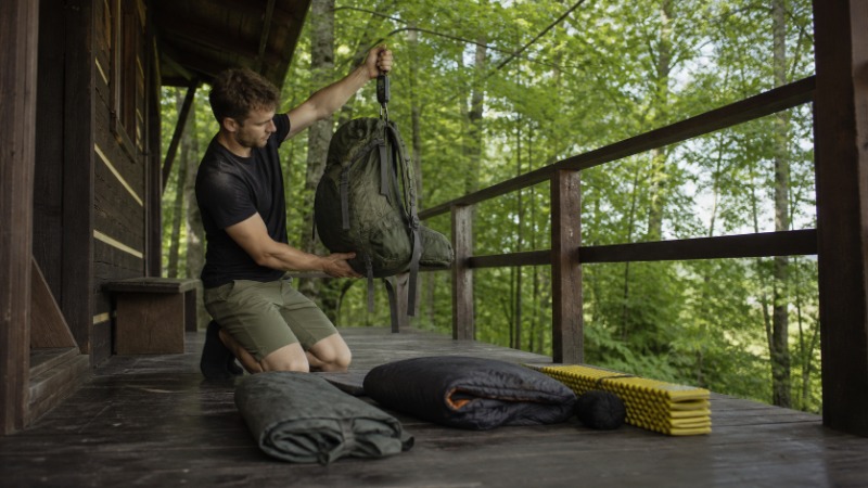 Rozložená turistická výbava na podlaze vedle otevřeného batohu a kuchyňské váhy
